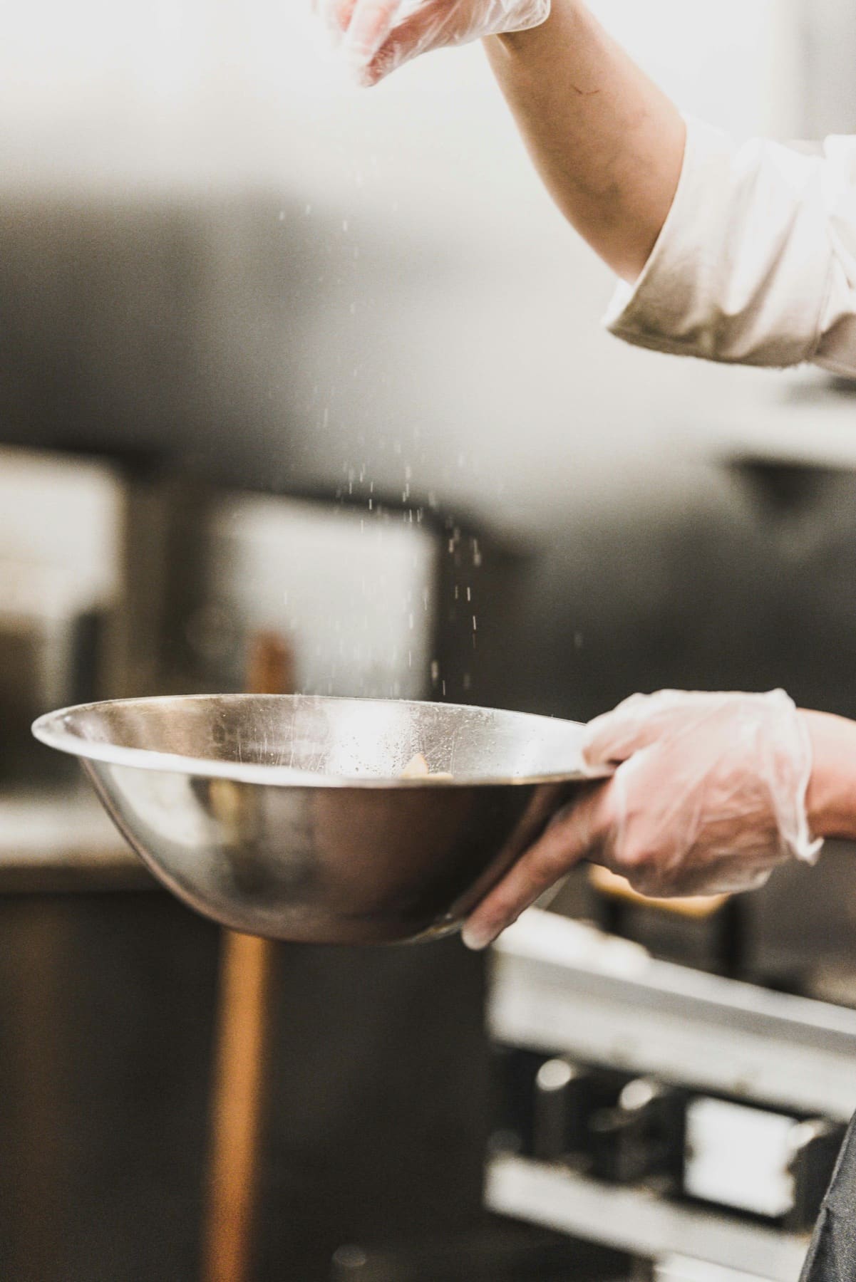 A chef sieving flour into a mixing bowl in a professional kitchen