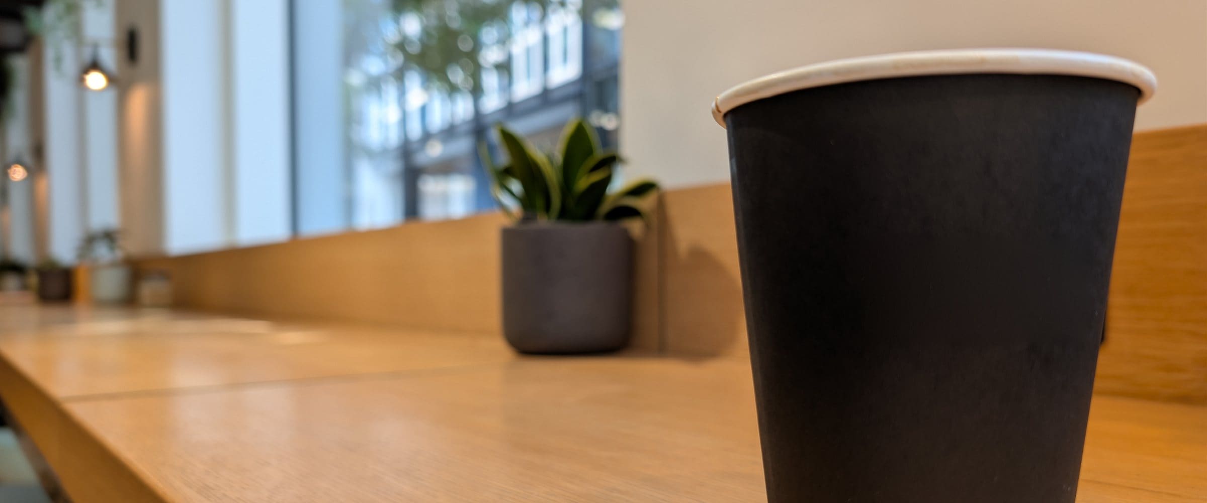 A takeaway coffee cup on the counter of a cafe window bar